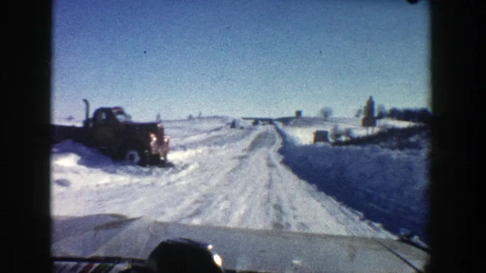 1961 Aspen 8mm frame showing a vehicle passing a dark parked truck beside a snow-covered mountain road.