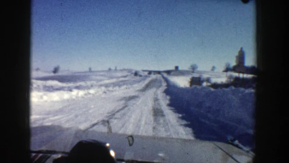 Forward-facing 1961 Aspen home-movie view of a snow-covered road with open winter landscape ahead.