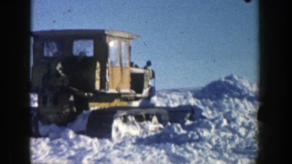 Side view of the yellow tracked snow plow moving beside high snowbanks in the 1961 Aspen winter footage.