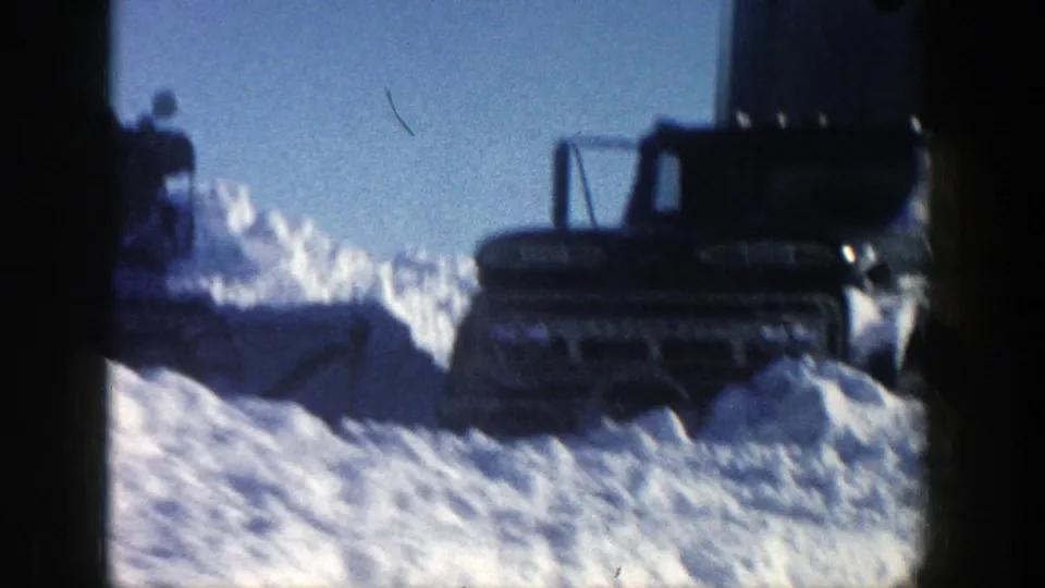 A tracked plow or parked vehicle appears partly in shadow behind deep snow in the Aspen winter scene.