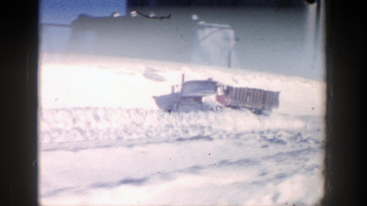 Red truck partly buried in deep snow beneath a bright sky.