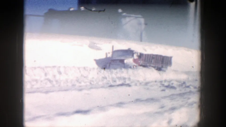 1961 Aspen, Colorado home-movie frame showing a red truck partly buried behind a high snowbank on a sunny winter day.