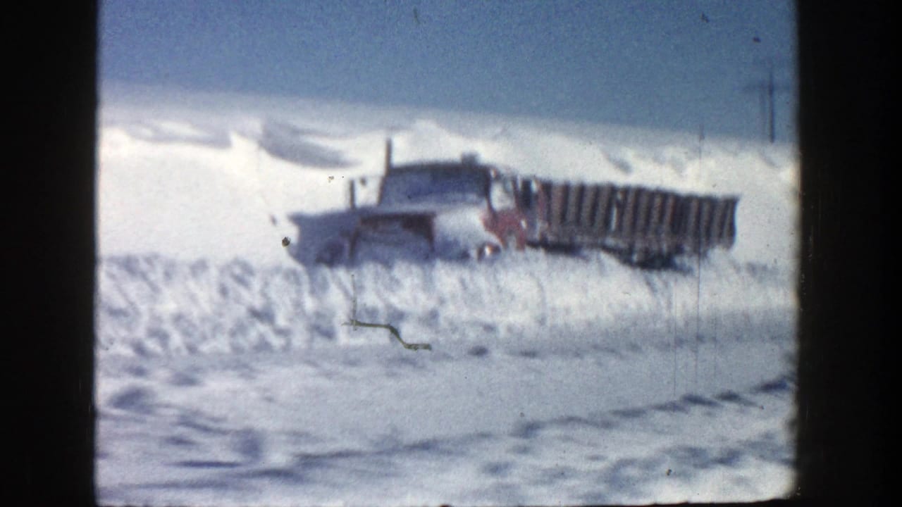 Red truck and long bed or trailer stuck beside tall snowdrifts.