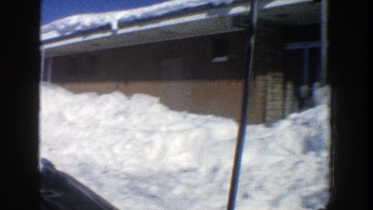 Snowbank beside a low brick building with a snowy roof.