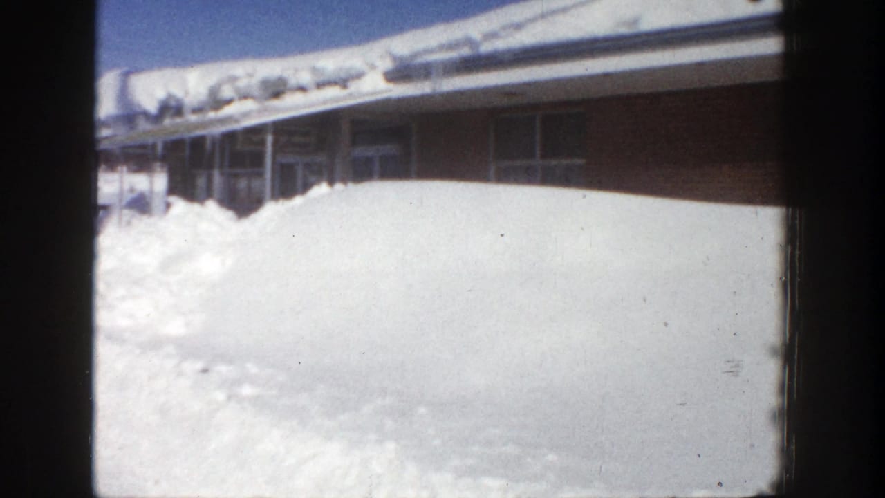 Snow wall fills the foreground beside a brick building and windows.