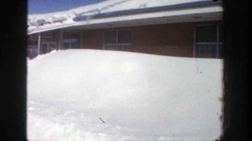 Aspen 1961 home-movie frame showing a tall, bright snowbank pressed up against the building windows.