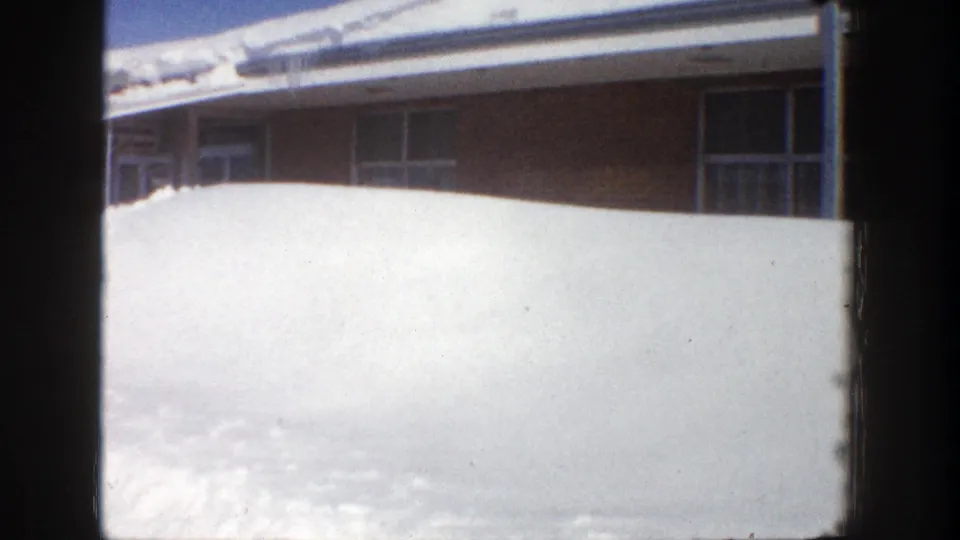 Final 1961 Aspen frame showing the broad snow wall covering the lower building frontage beneath dark window frames.