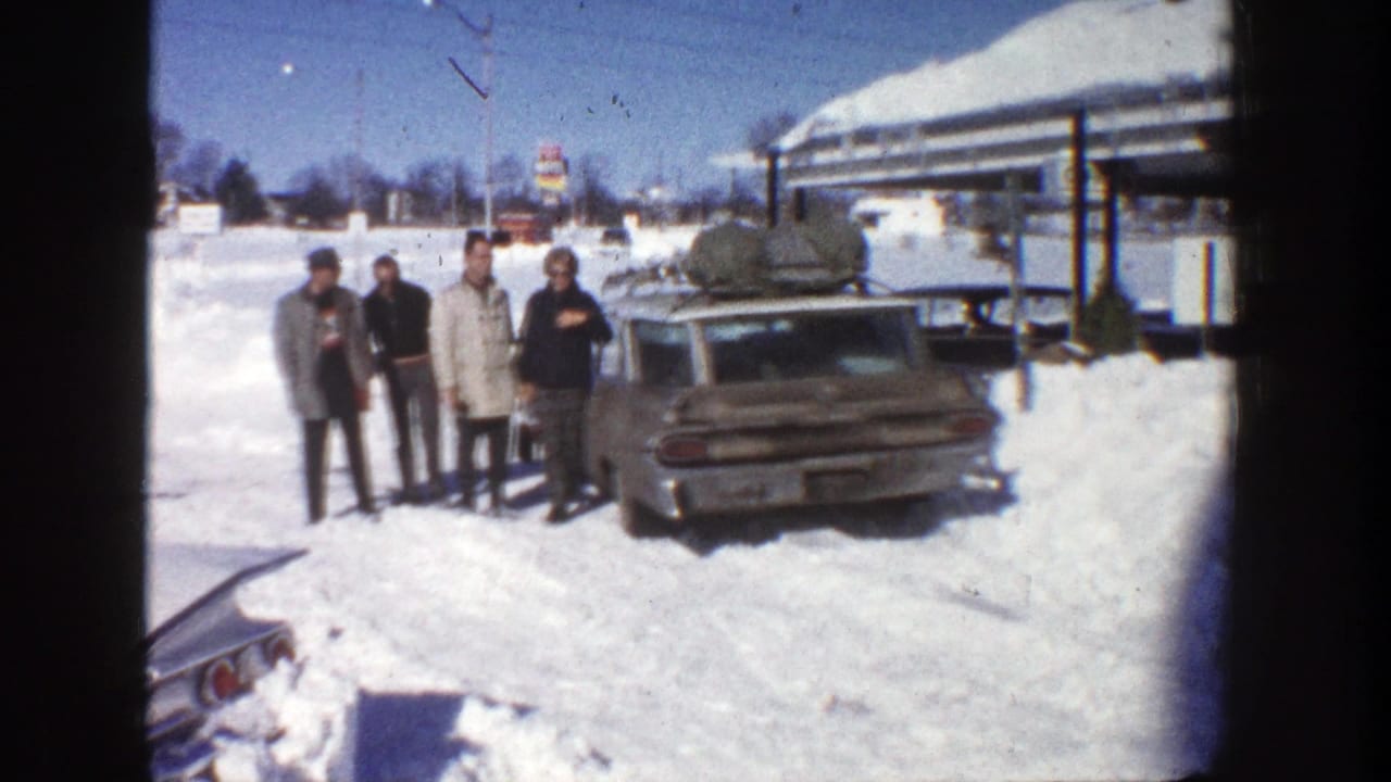 Four adults stand in deep snow beside a station wagon with roof luggage.
