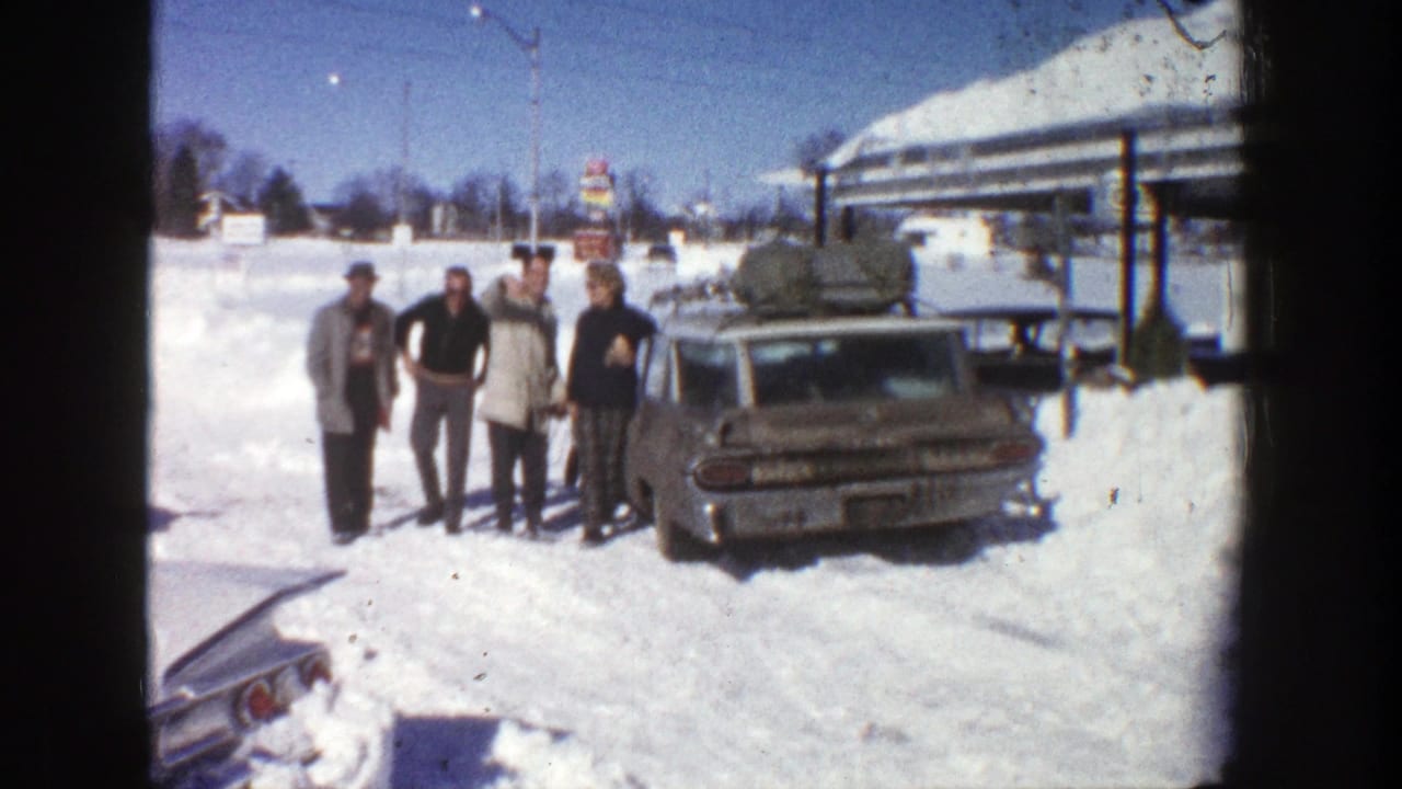 Four adults stand closer together beside the rear of a station wagon in snow.