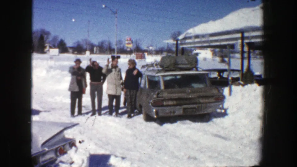 The family group continues facing the camera beside the loaded station wagon in the snowy Aspen parking lot.