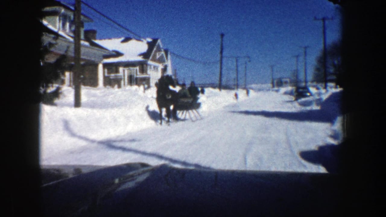 Horse-drawn sleigh travels down a snowy street past houses and high snowbanks.