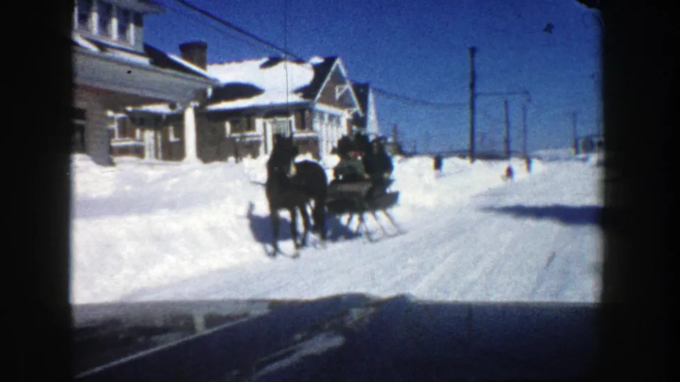 A horse-drawn sleigh with passengers passes snow-laden residential houses on an Aspen street in this 1961 8mm home-movie frame.