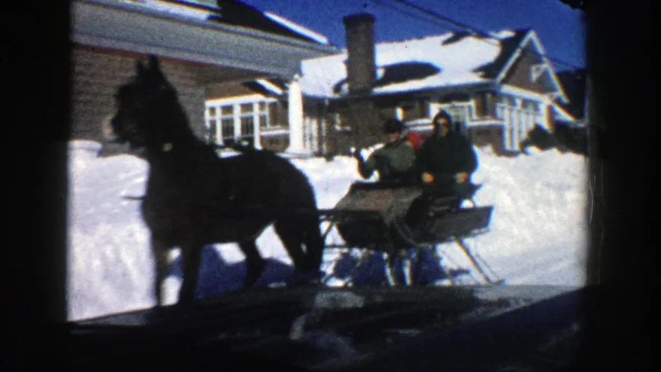 Close view of a dark horse and sleigh carrying bundled passengers on a snowy Aspen residential street in 1961.