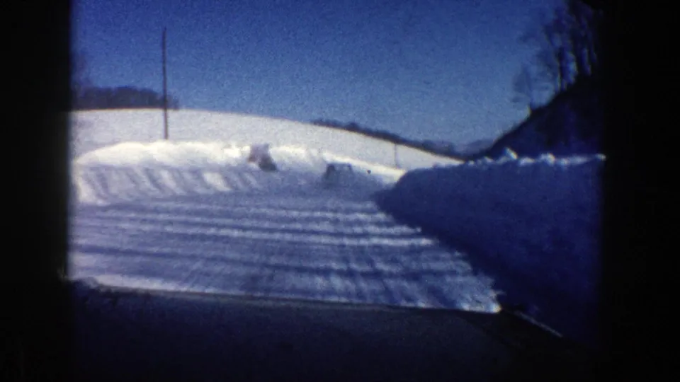 1961 Aspen, Colorado car view of a snow-covered road with deep plowed banks, open hills, and a utility pole under clear sky.