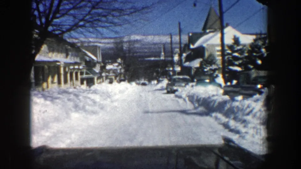 1961 Aspen winter street scene from a car, showing snowbanks, houses, bare trees, utility lines, and distant mountain slopes.