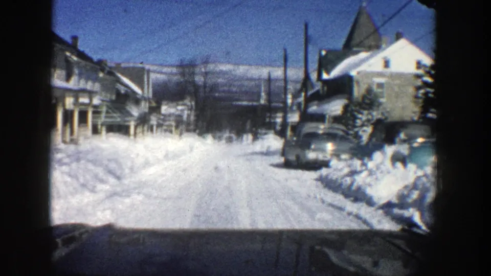 Aspen, Colorado winter street view from 1961 showing a parked car, snow-covered houses, utility poles, and distant hills.