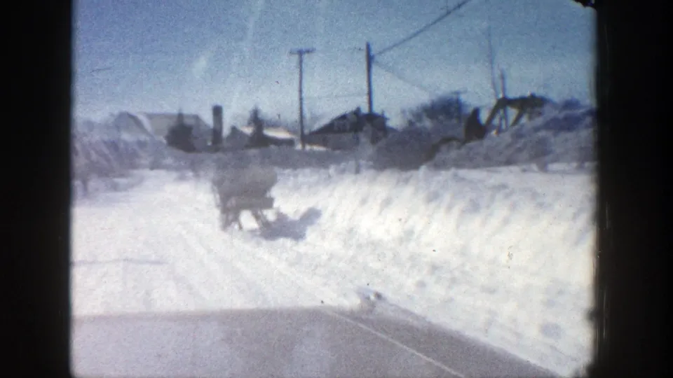 1961 Aspen road view shows a horse-drawn sleigh entering the frame beside deep snowbanks and roadside utility poles.