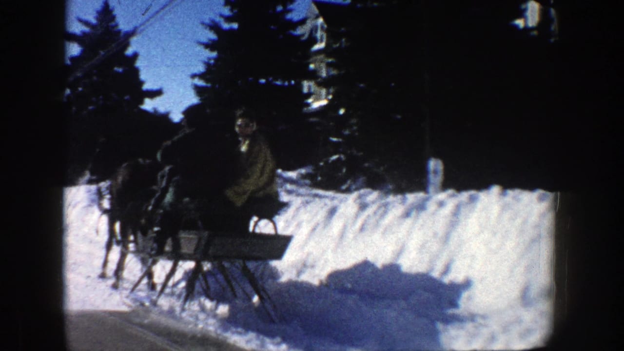 1961 Aspen 8mm frame showing a horse-drawn sleigh carrying passengers past snowbanks and evergreen trees.