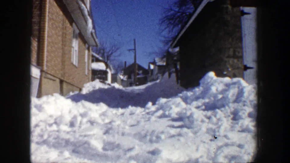 Final 1961 Aspen frame showing a snow-packed residential lane bordered by houses, trees, and utility lines.