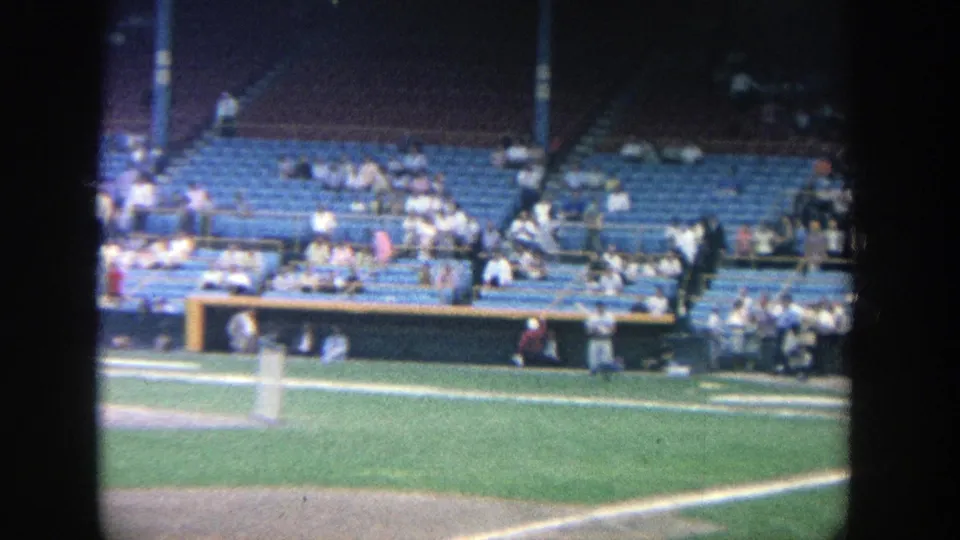 Spectator-shot 8mm view at Yankee Stadium in 1964 with blue seats, fans, and the edge of the baseball field visible.
