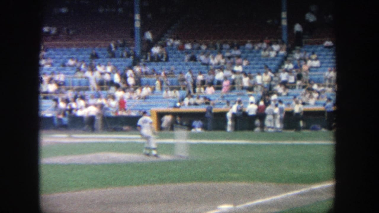 1964 Yankee Stadium home-movie frame showing a pitcher on the mound and a half-empty seating section in daylight.