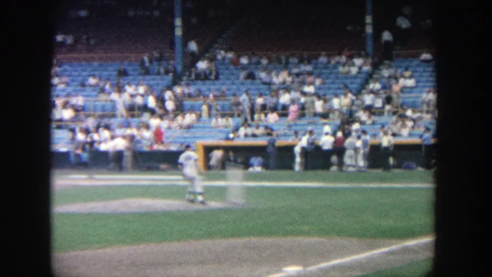 1964 Yankee Stadium home-movie frame showing a pitcher on the mound and a half-empty seating section in daylight.