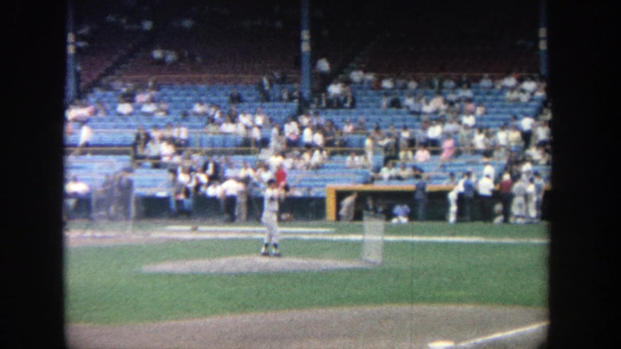 Pitcher and infield area seen from the stands with spectators in blue seats.