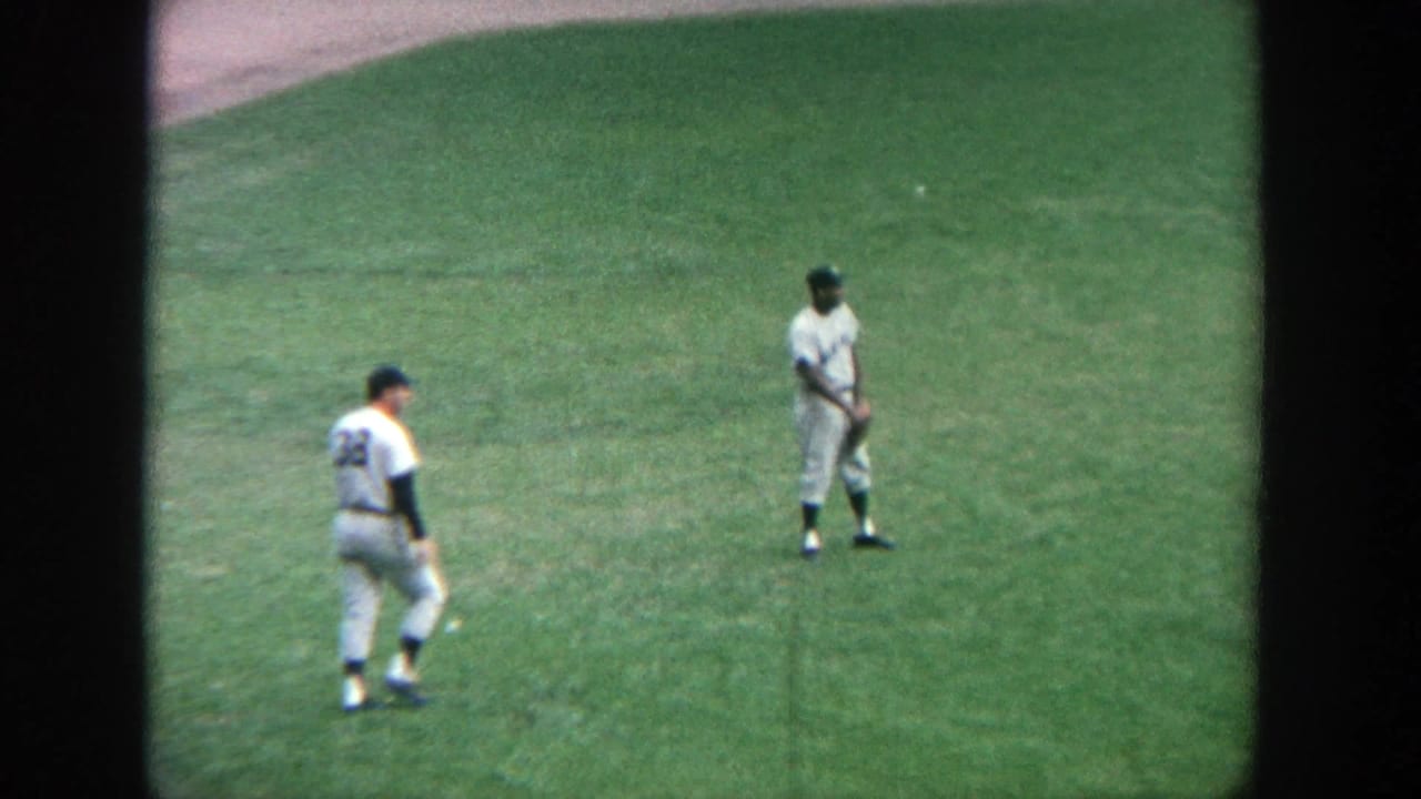 Two baseball players in white uniforms stand on the green outfield grass.