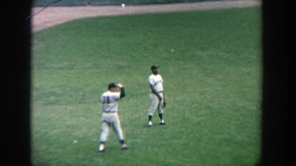 1964 Yankee Stadium frame showing one player lifting his glove or arm while another stands ready in the outfield.