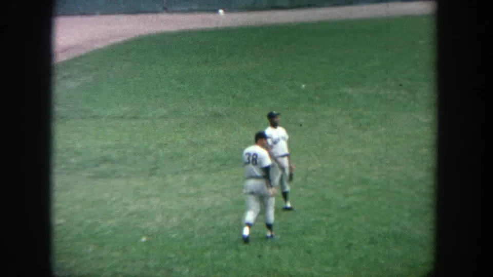 1964 Yankee Stadium home-movie frame with two players in white uniforms standing together on the green field.