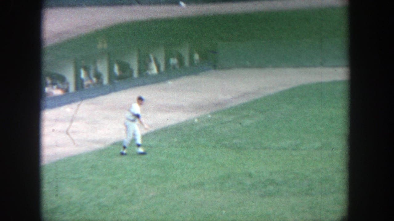 Uniformed baseball player walking across the outfield near stadium seating.