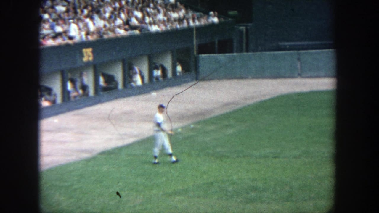 Uniformed player at Yankee Stadium in 1964 walking on the outfield grass near dugout openings and a crowded stand.