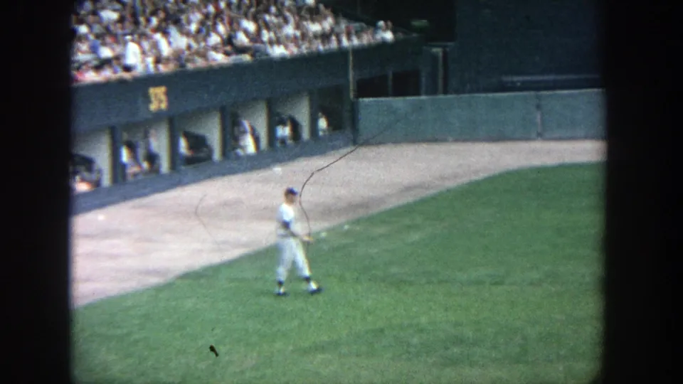 Uniformed player at Yankee Stadium in 1964 walking on the outfield grass near dugout openings and a crowded stand.