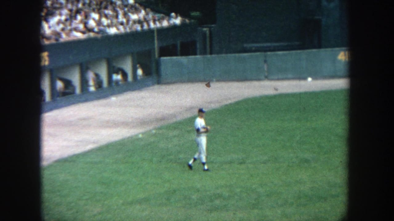 1964 Yankee Stadium frame showing a player crossing the outfield below the stands, filmed from a spectator viewpoint.