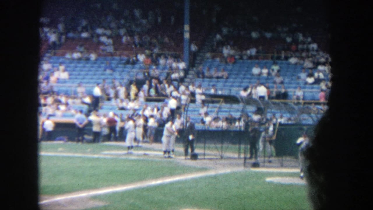 Yankee Stadium pre-game practice seen from the stands, with uniformed players near the dugout and fans in blue seating.