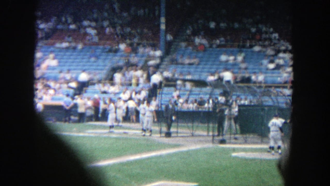 Baseball players and officials near home plate with blue stadium seats behind them.