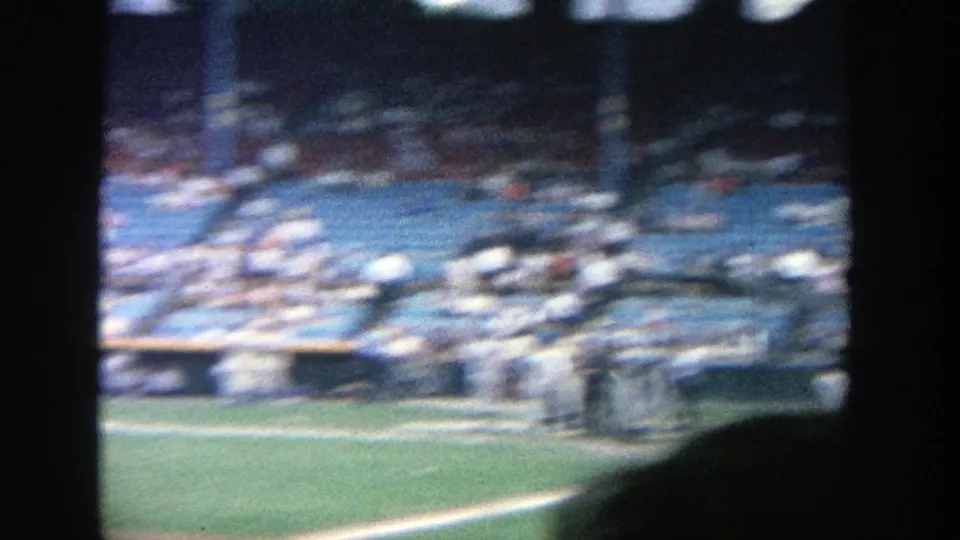 Soft, motion-blurred 1964 Yankee Stadium frame showing the mound, nearby players, and spectators in blue stadium seating.