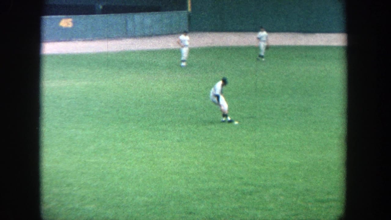 1964 Yankee Stadium view from the stands, with players in white uniforms positioned across the green outfield.