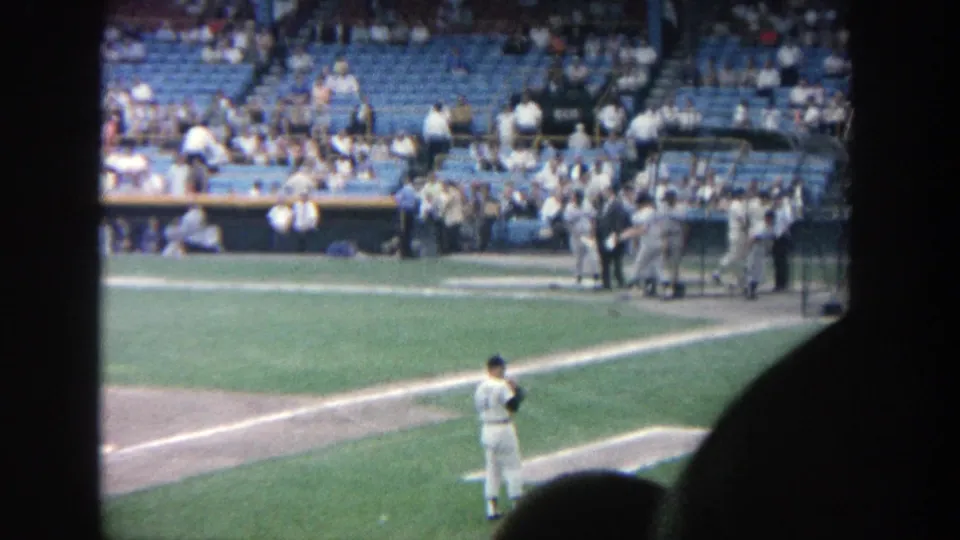 1964 Yankee Stadium spectator footage showing the pitcher paused on the field while players gather near the dugout.