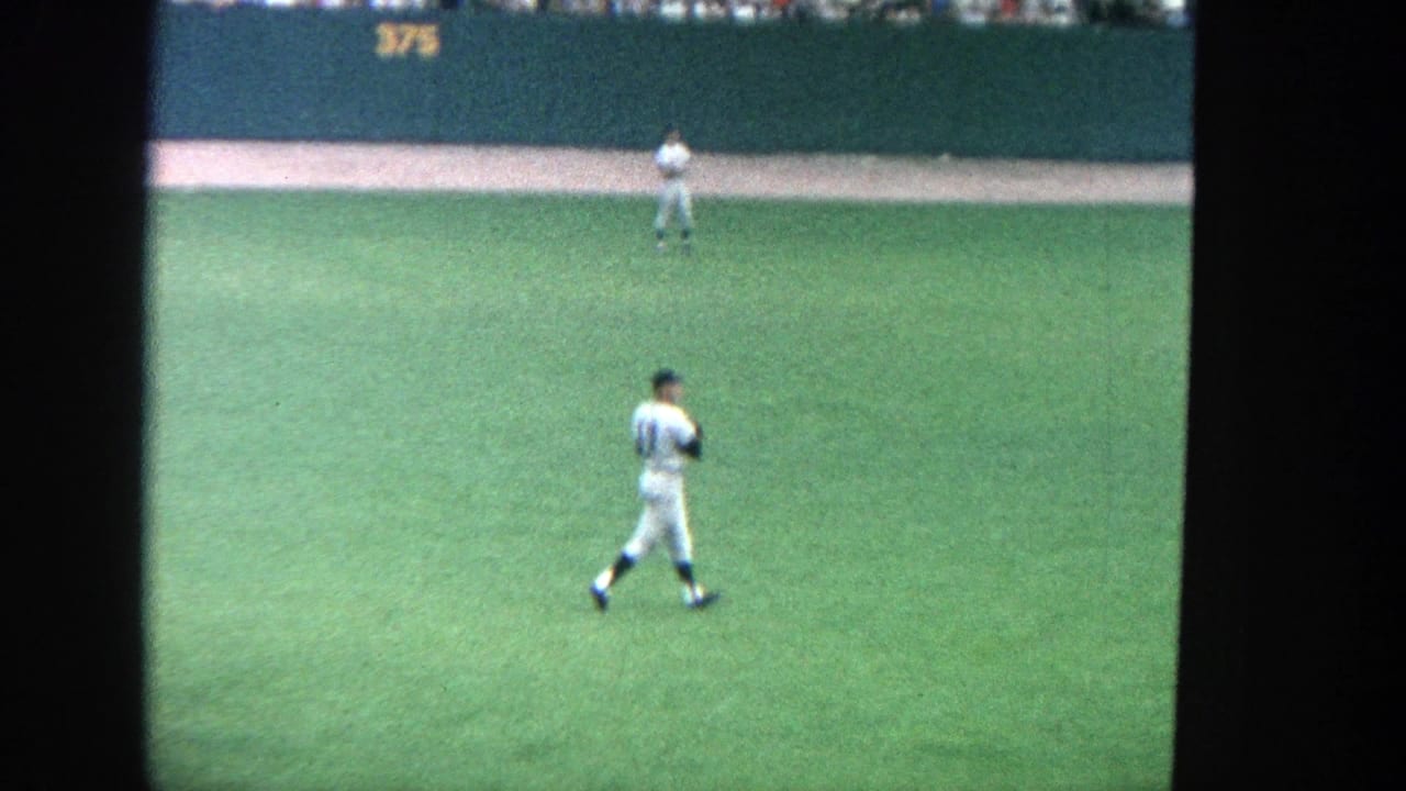 1964 Yankee Stadium outfield view with a white-uniformed player on the grass, another near the wall, and spectators above the 375 marker.
