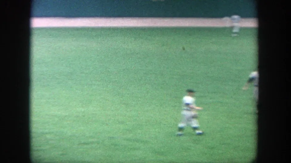 Soft 8mm frame from the 1964 Yankee Stadium game showing a player moving across the outfield with the warning track behind him.