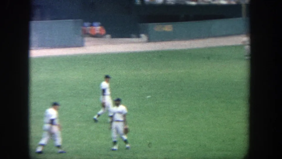 1964 Yankee Stadium outfield scene with several players in white uniforms walking or standing near the wall and warning track.