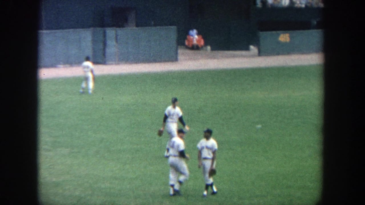 Baseball players in white uniforms walking and throwing on the outfield grass.
