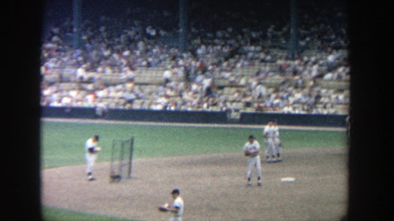 1964 Yankee Stadium frame showing players on the infield dirt and grass, with spectators visible across the seating bowl.