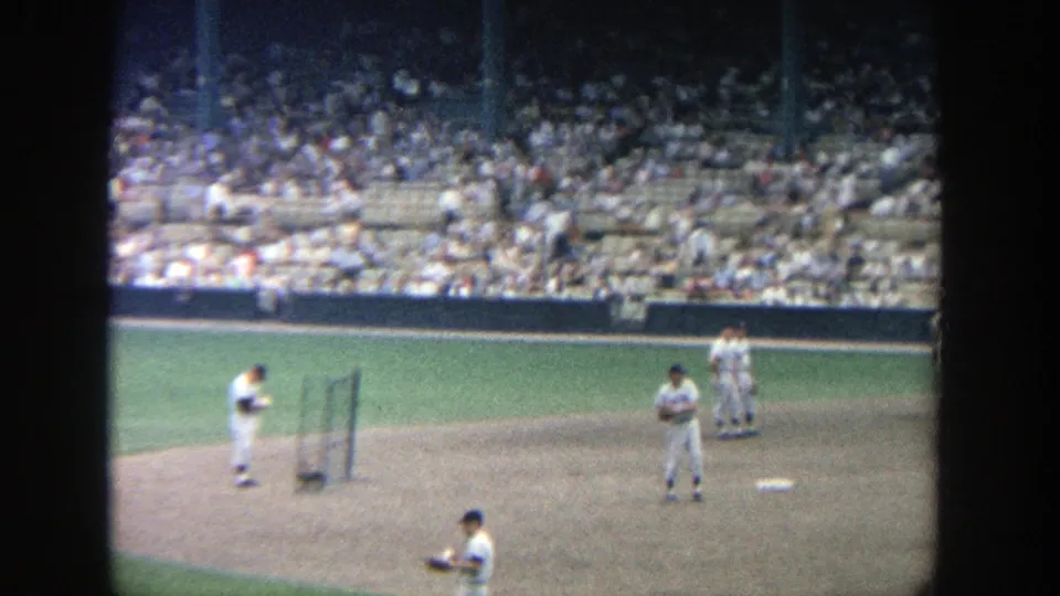 1964 Yankee Stadium frame showing players on the infield dirt and grass, with spectators visible across the seating bowl.