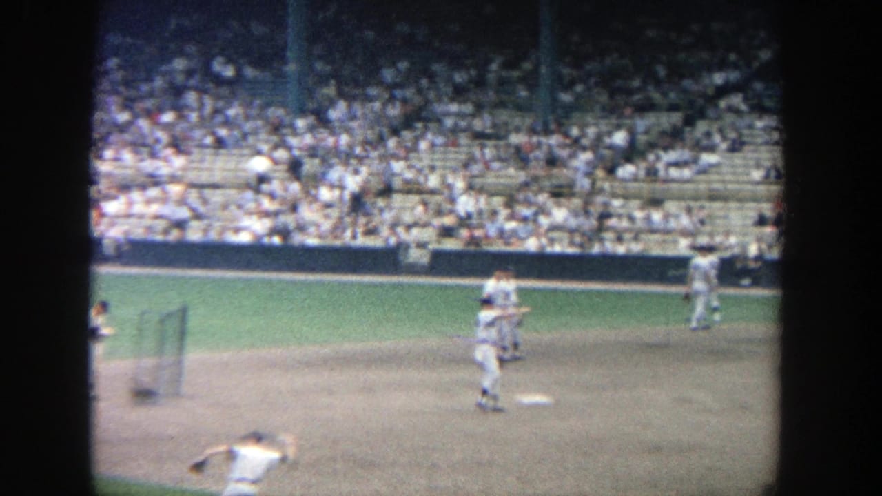 Baseball players warming up on the infield with spectators seated behind them.