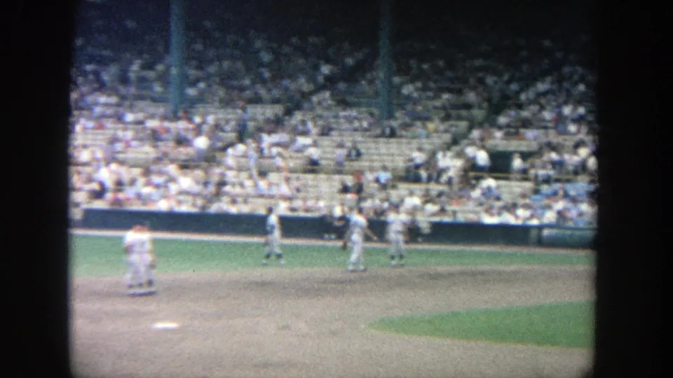 A soft 8mm frame shows players spread across the Yankee Stadium infield area, with spectators filling rows behind them.