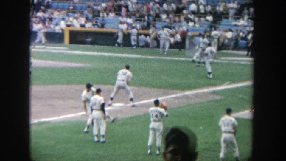 From the stands at Yankee Stadium, several players gather near the baseline and dugout area while one spectator silhouette appears in the foreground.