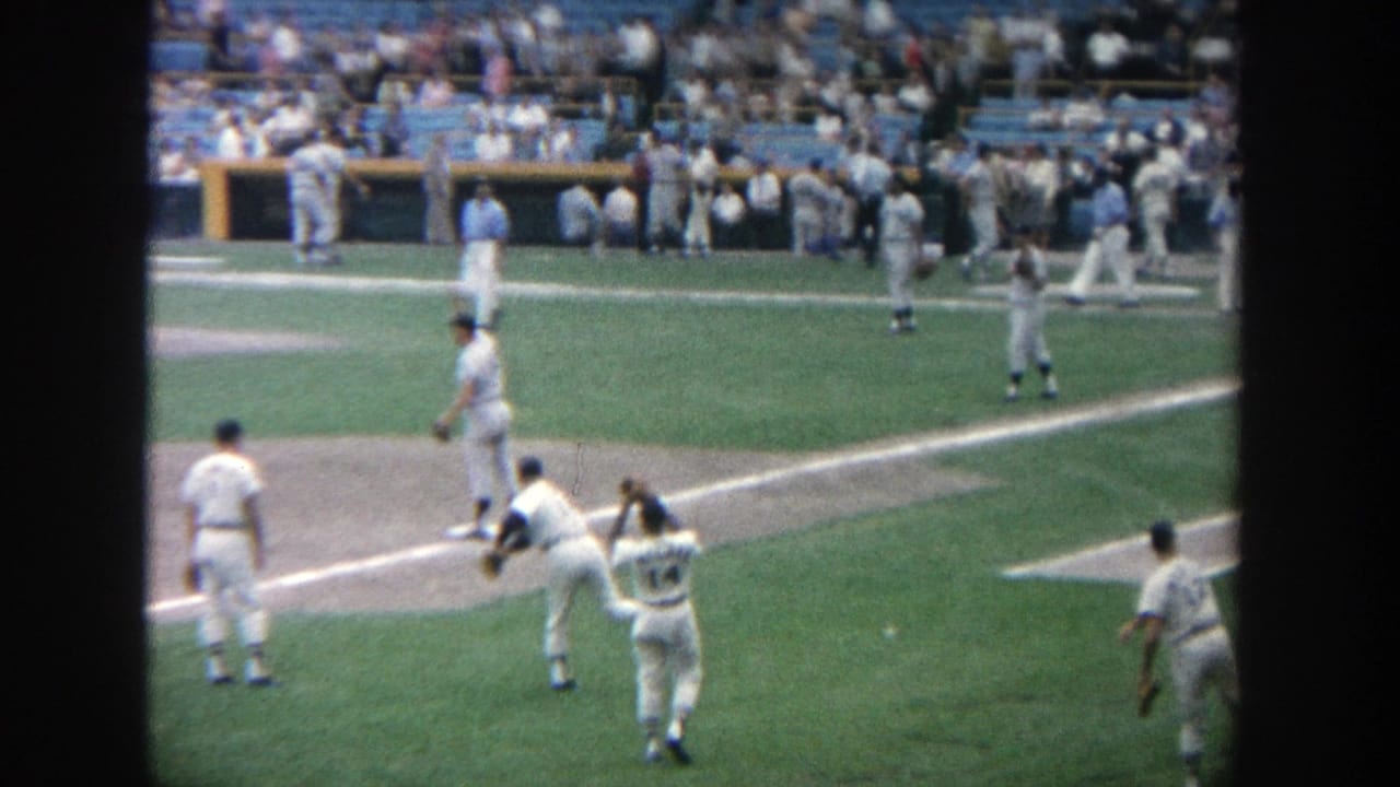 1964 Yankee Stadium home-movie frame showing baseball players throwing and fielding on the grass before a game.