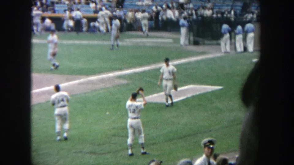 1964 Yankee Stadium home-movie view of uniformed players warming up near the foul line with spectators in the background.
